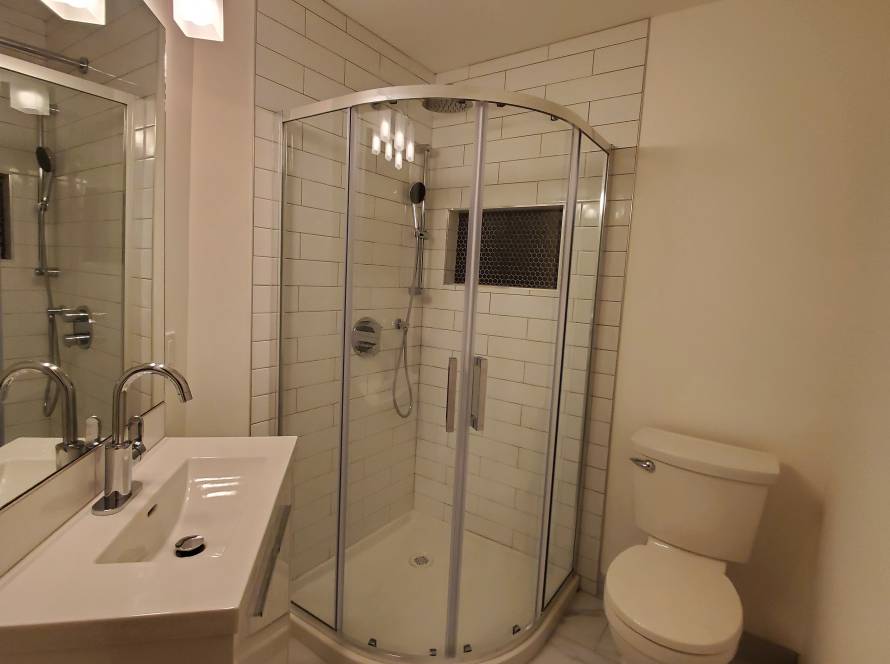 Renovated bathroom with a curved glass corner shower, white wall tile and marble-look floor tile
