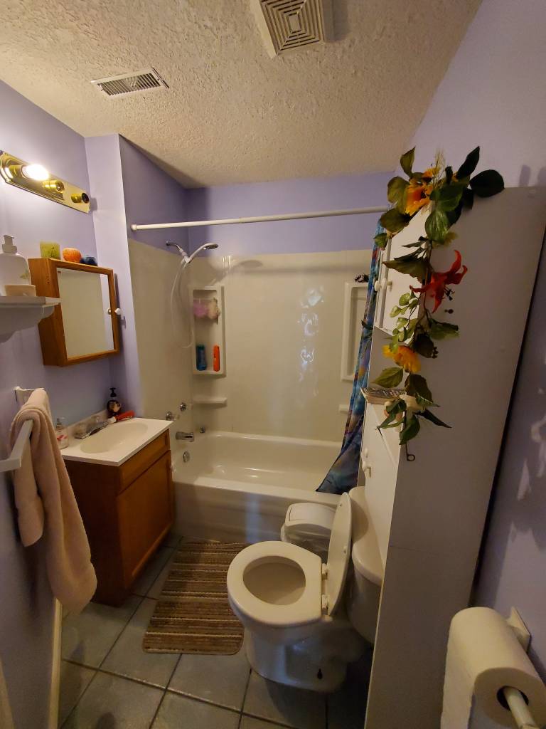 Small bathroom before renovation with a wood vanity, tub and older finishes